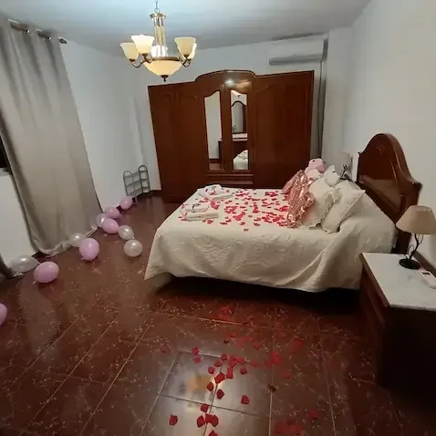 Detalles cuidados para que tu celebración sea perfecta desde el primer momento. Habitación decorada con pétalos de rosa, globos y una cama con sábanas claras.
