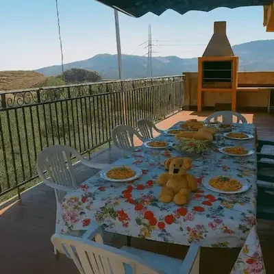 Terraza de Cortijo Terrón con comedor Mesa al aire libre con platos de comida y un oso de peluche en un entorno montañoso.
